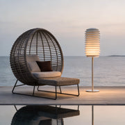 LED light bollard with a modern design, placed beside a wicker chair by the seaside.