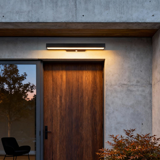 Modern LED linear wall light installed above a wooden front door, casting warm downward illumination and enhancing the minimalist exterior.