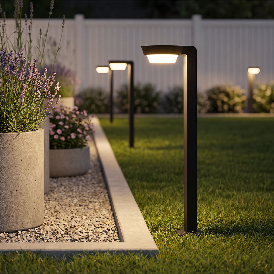LED path lighting lining a landscaped garden edge, featuring modern black bollard lights with warm illumination beside a gravel border and lawn.