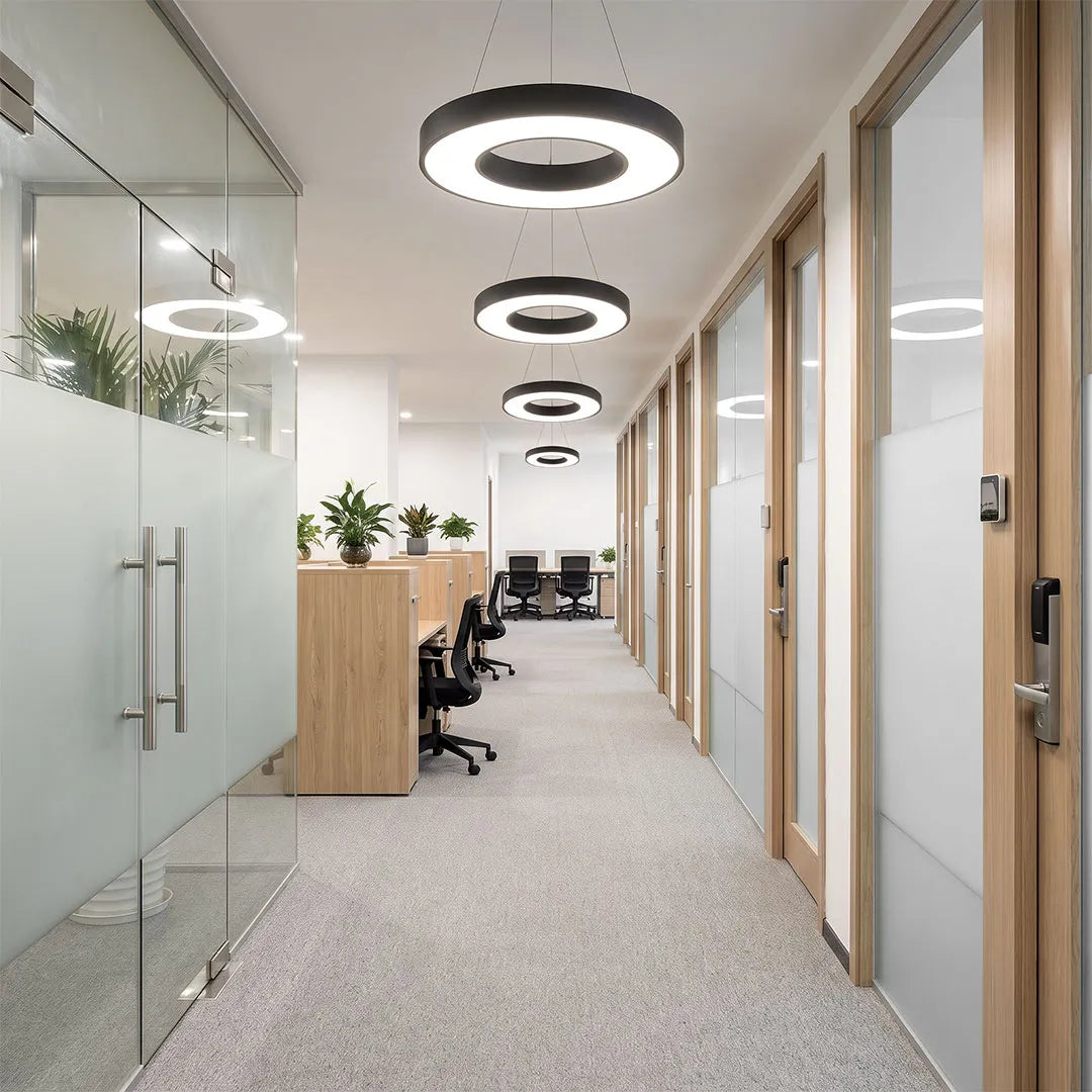 LED pendant ring ceiling light illuminating a modern office hallway with glass partitions and wood accents.