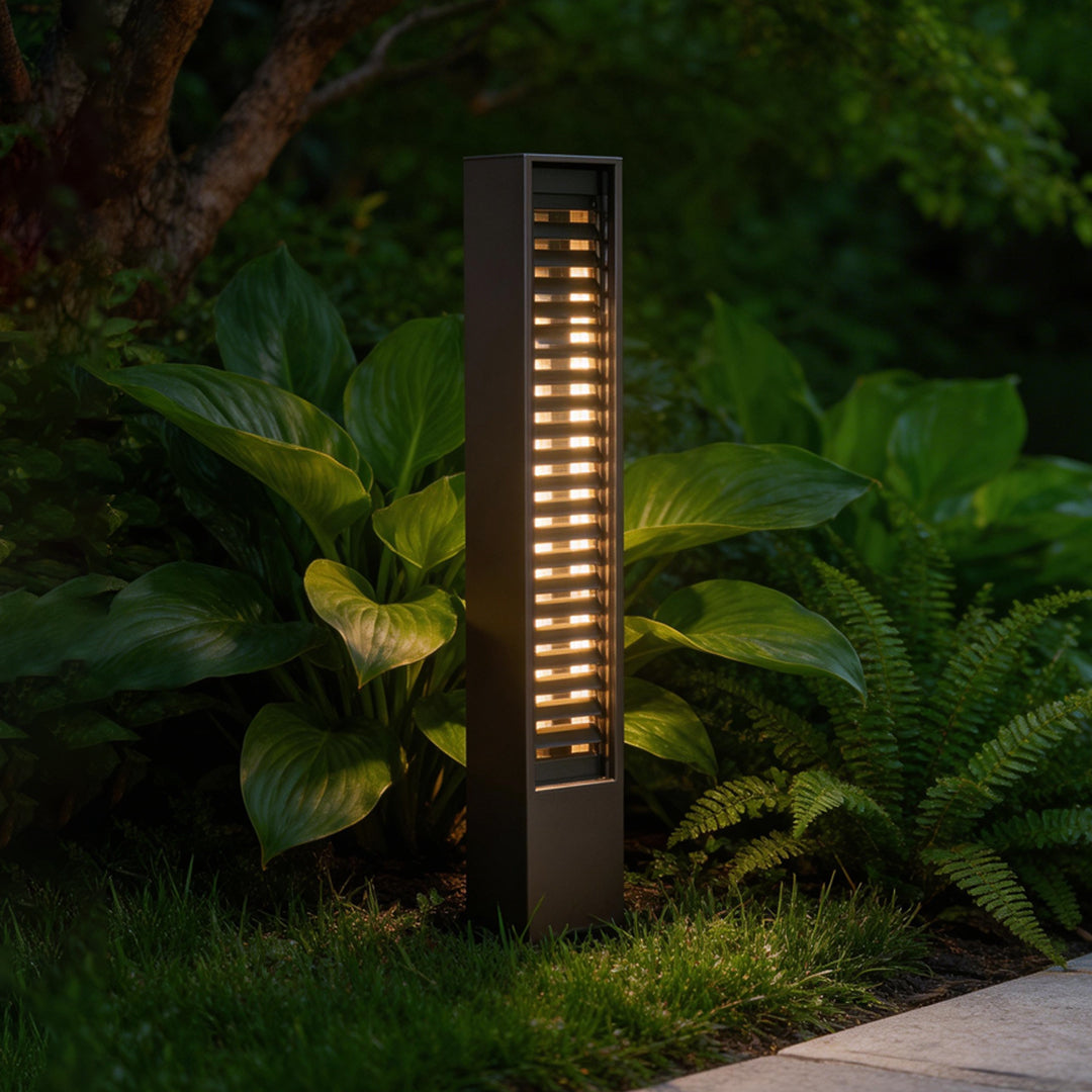 LED wall sconce outdoor used as bollard lighting in garden, modern pathway light illuminating plants with warm glow.