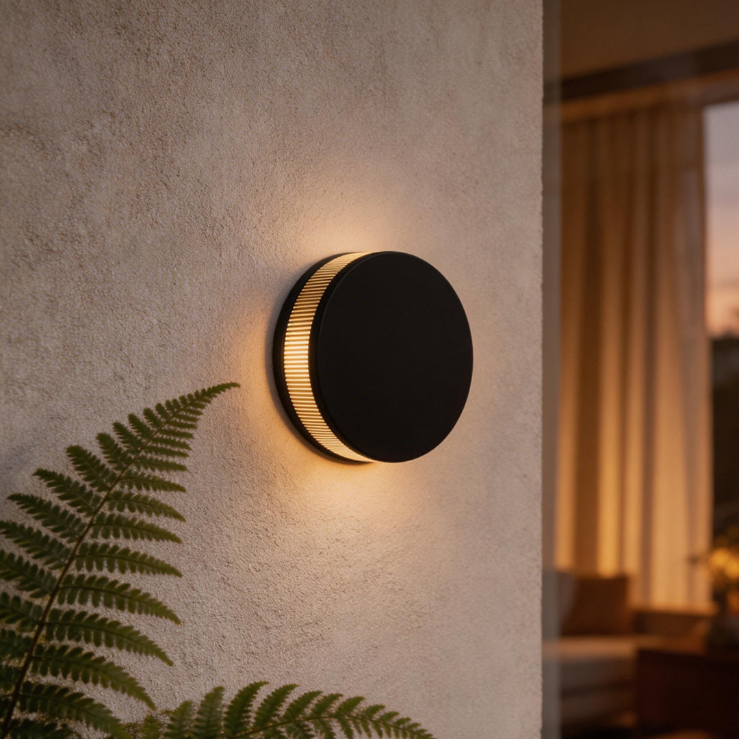LED wall sconce outdoor round black fixture on stucco wall, warm halo glow creating modern exterior ambiance.