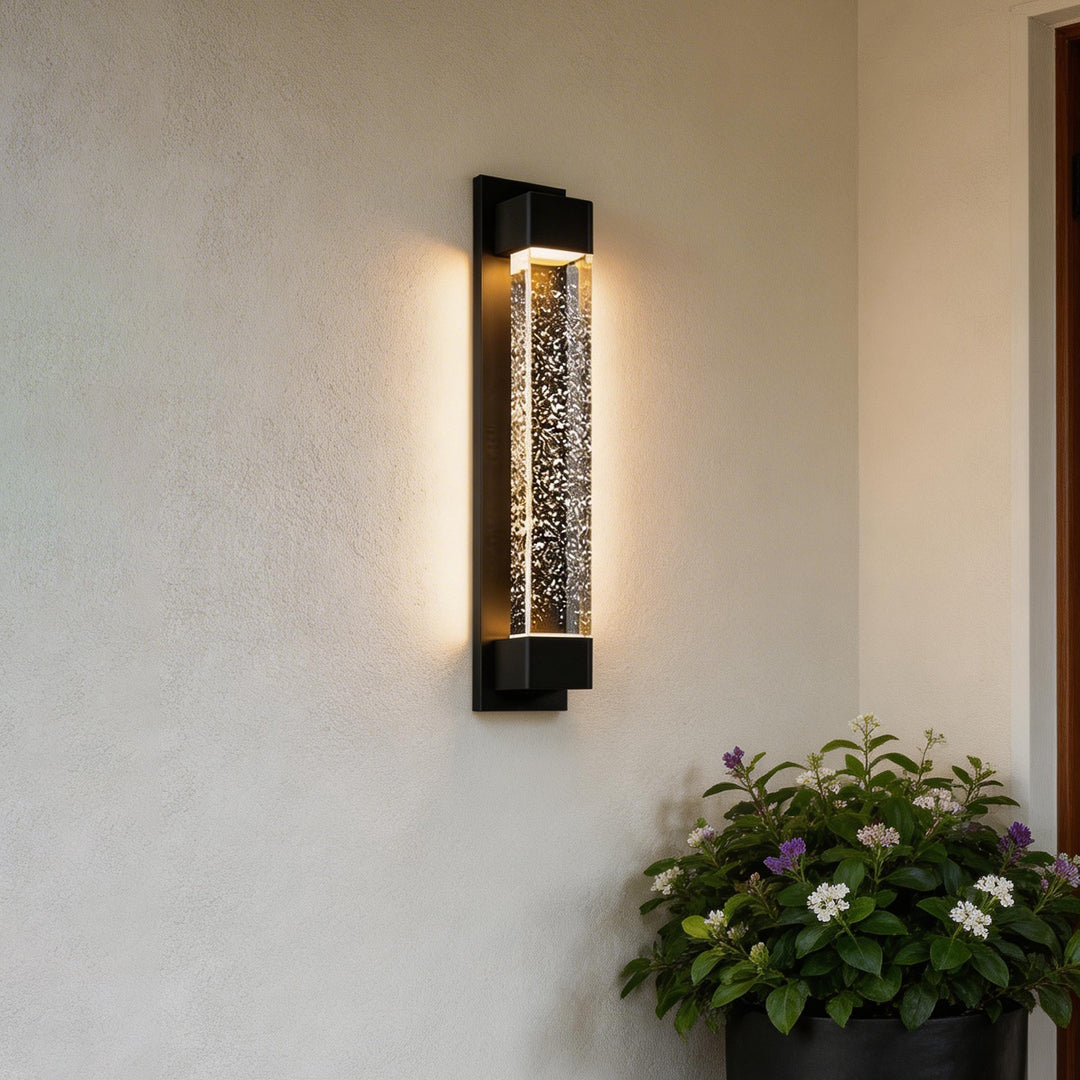 LED wall sconce outdoor on stucco wall, sleek black fixture with warm glow and textured bubble glass design.