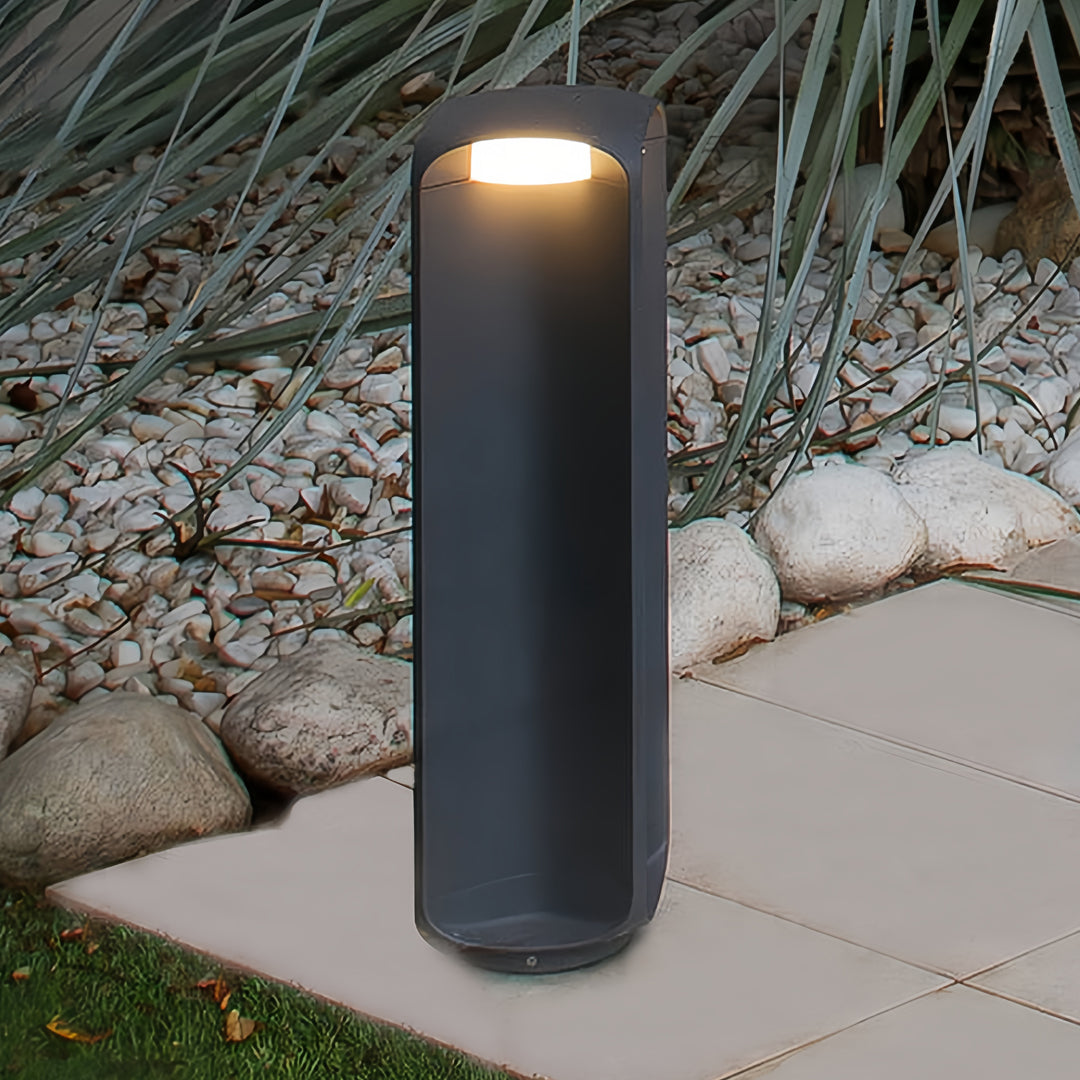 Single standing light bollard illuminating a stone garden pathway in an outdoor setting.