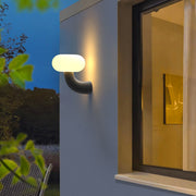Illuminated light outdoor wall sconce mounted on an exterior wall, casting warm light near a window.