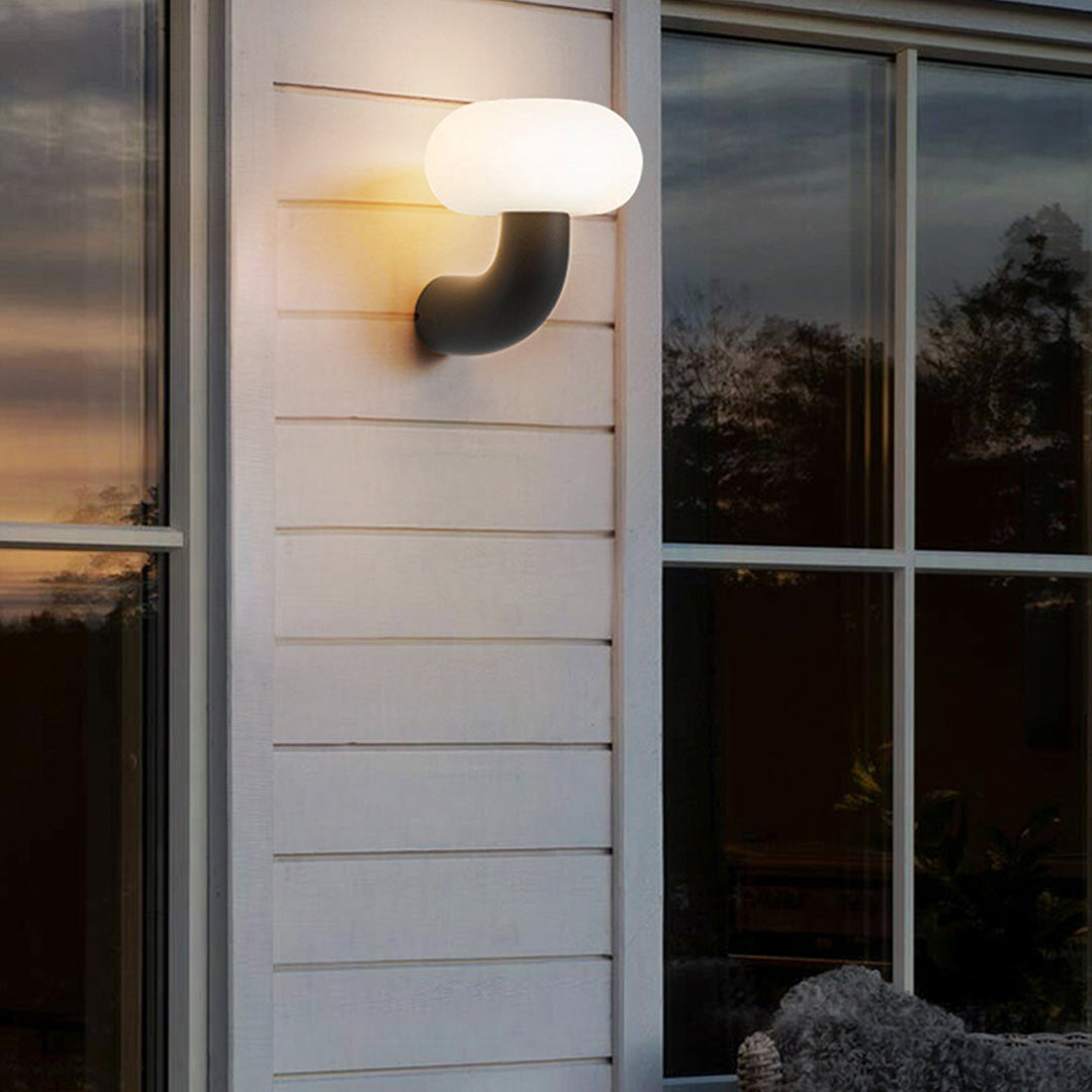 Warm glowing light outdoor wall sconce installed beside a window on a wooden exterior wall at dusk.