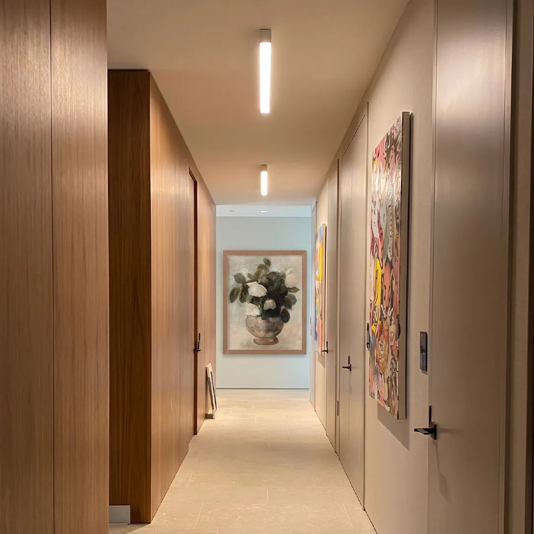 Linear ceiling lights illuminating a long modern corridor with wood paneling and framed artwork.