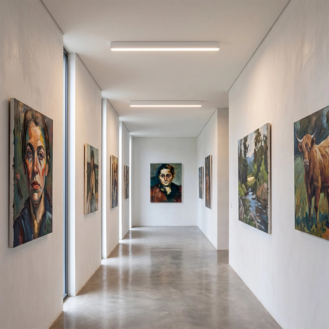 Linear ceiling light mounted in a minimalist white hallway, creating clean and even lighting along a modern corridor with artwork.
