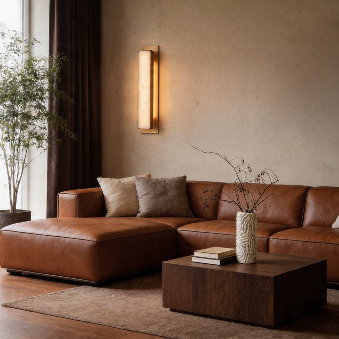 Linear gold wall light fixture glowing above a brown leather sectional sofa in a modern lounge.