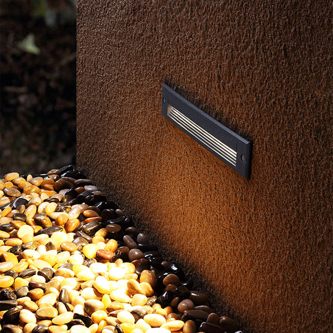 Linear ground light fixture creating warm illumination on stone pathway and garden area