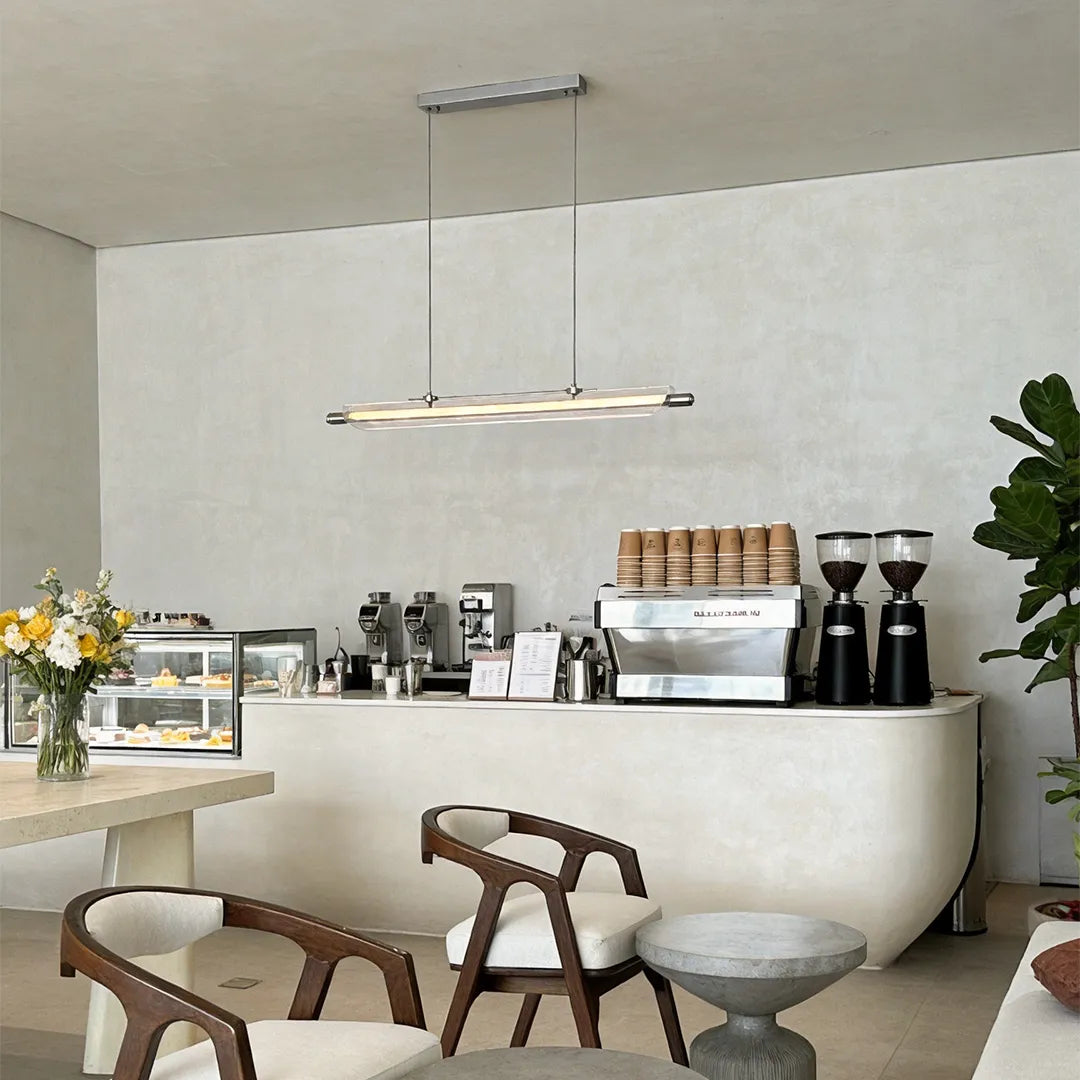 Linear LED pendant light suspended over a modern cafe bar with curved counters and neutral decor.