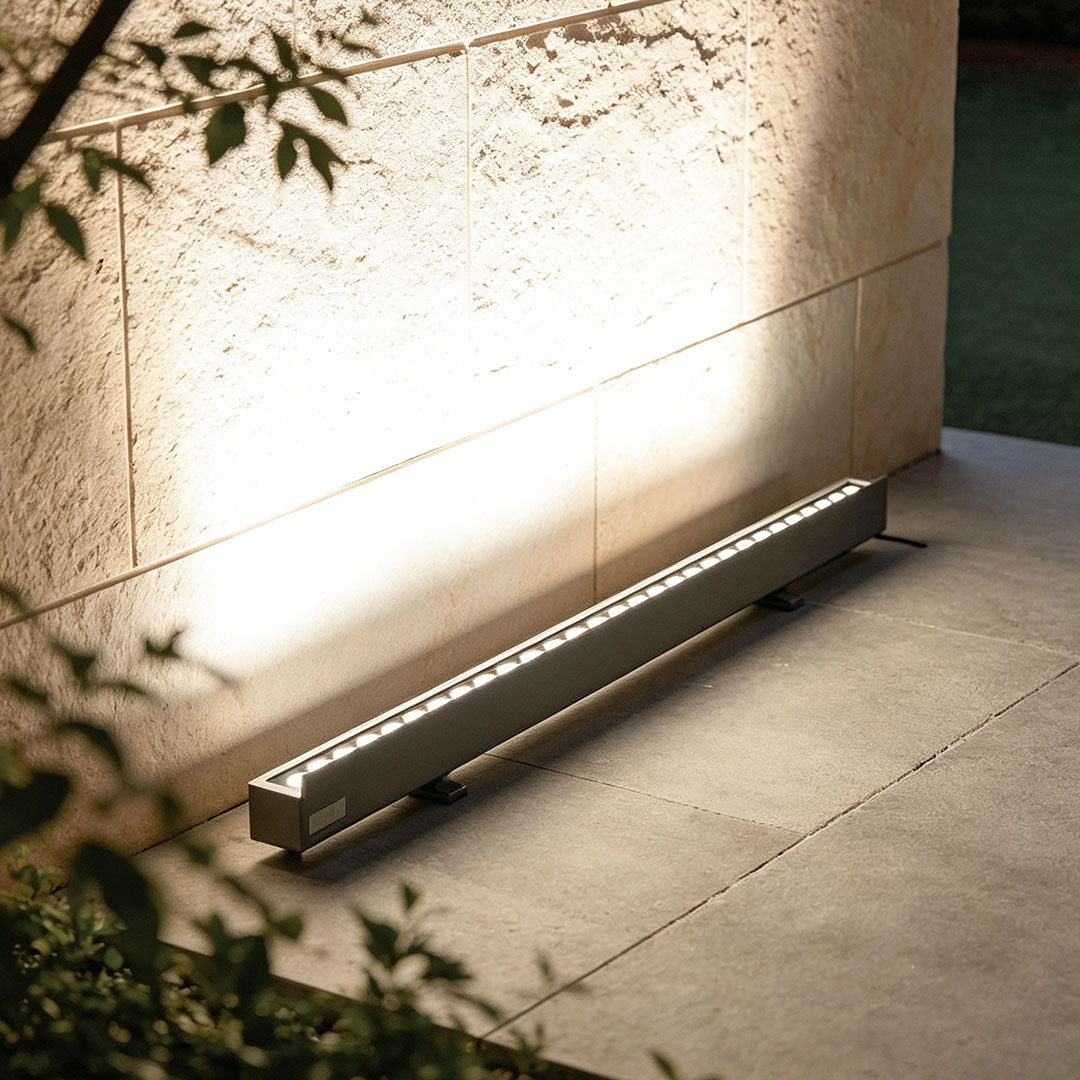 Linear LED wall washer mounted at the base of an exterior wall, casting even upward illumination across the surface.