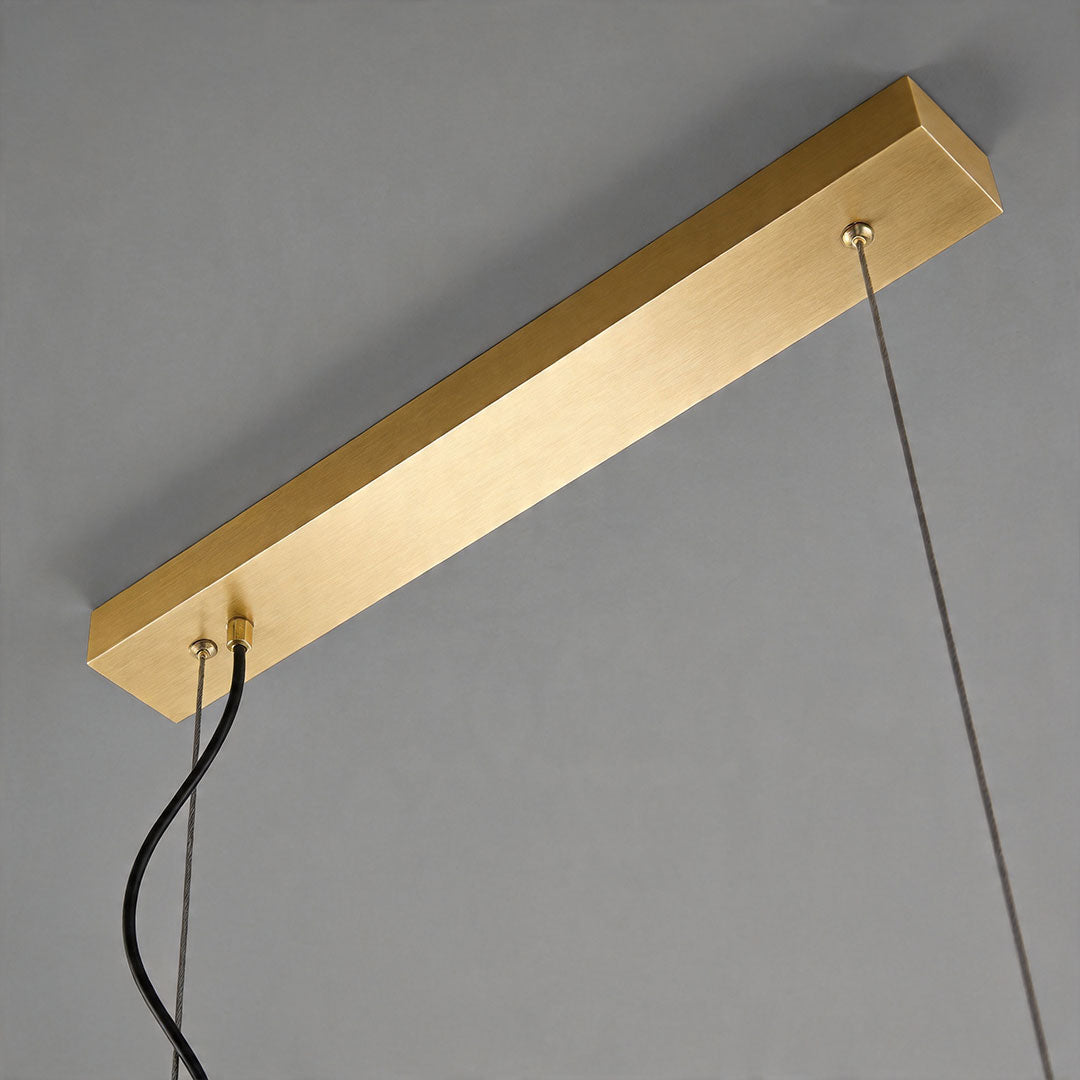 Ceiling canopy detail of linear modern chandelier with rectangular gold mounting plate and suspension cables.