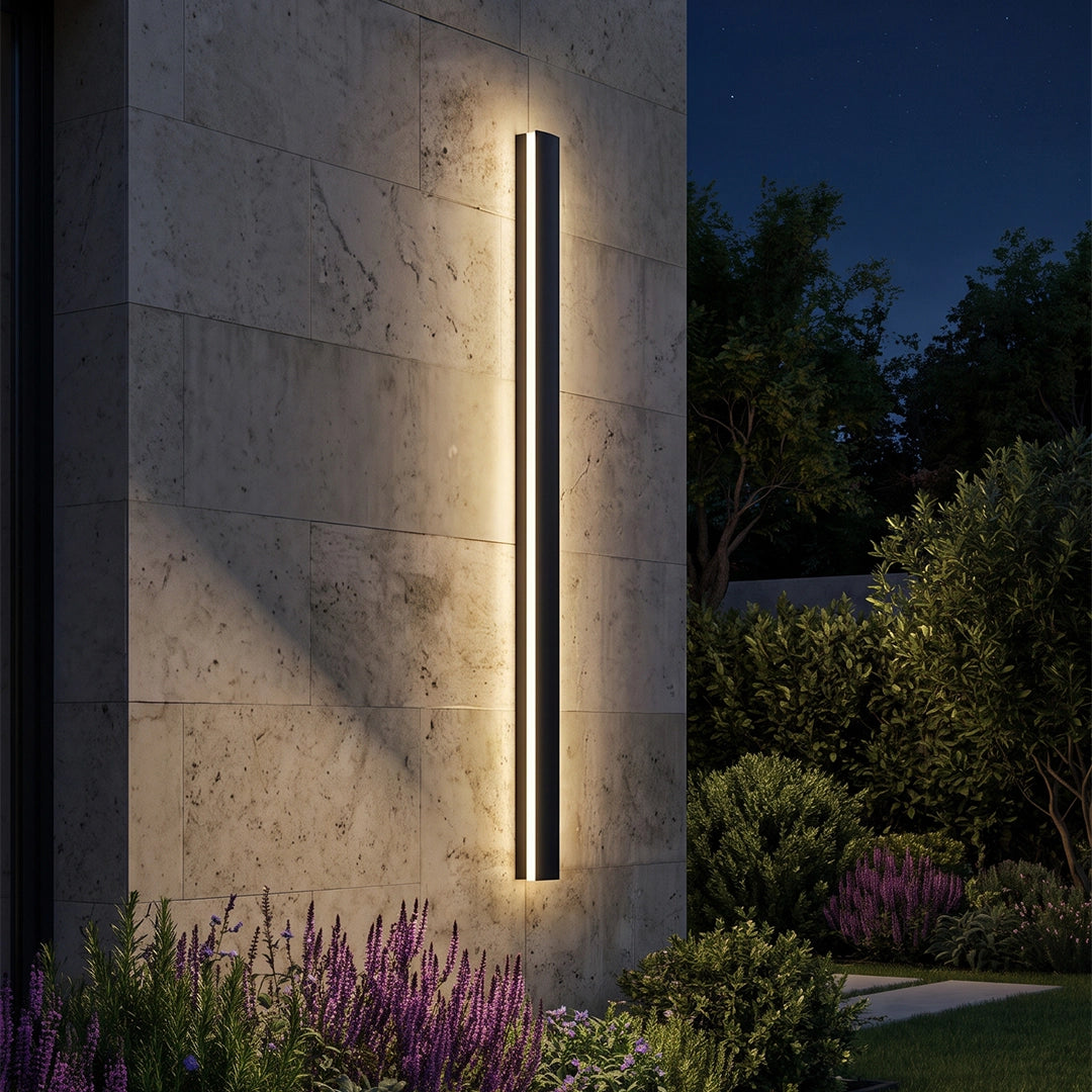 Close-up of a linear outdoor wall sconce glowing on a textured stone wall at night.