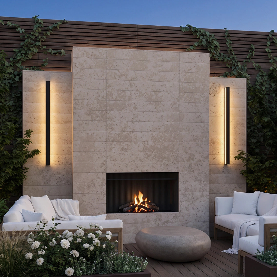 Linear outdoor wall sconces flanking an outdoor fireplace on a stone patio wall.