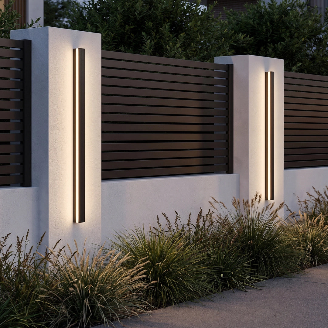Linear outdoor wall sconces installed on white garden walls beside a horizontal slat fence.