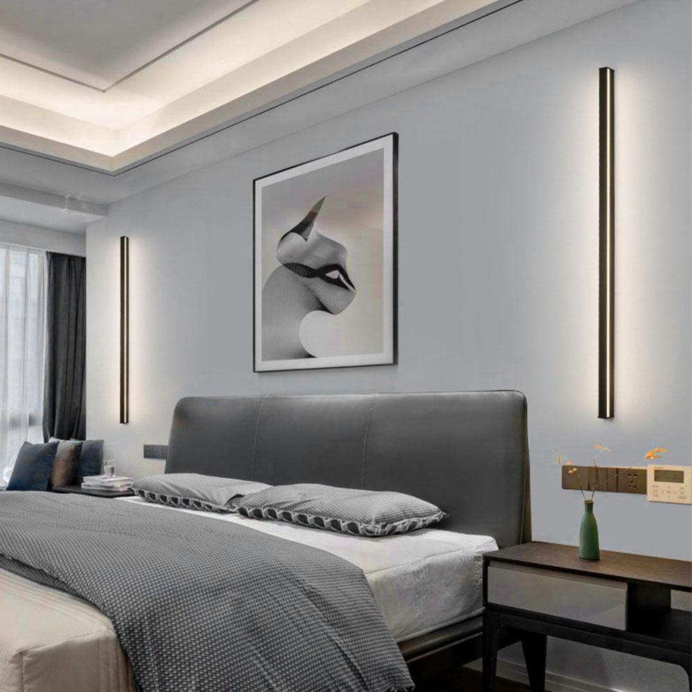 Linear outdoor wall sconce providing warm illumination, mounted on a stone wall beside a cozy outdoor seating area.