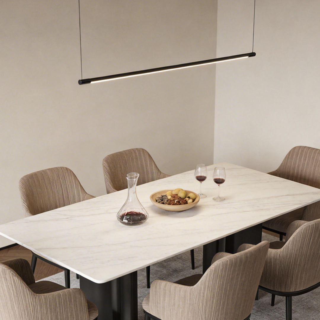 Linear pendant light fixture installed above dining table with minimalist interior style.