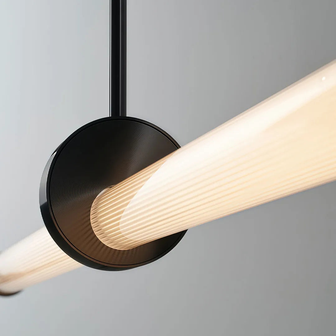 Close-up of linear pendant lights with a black circular mount and ribbed glowing tube.