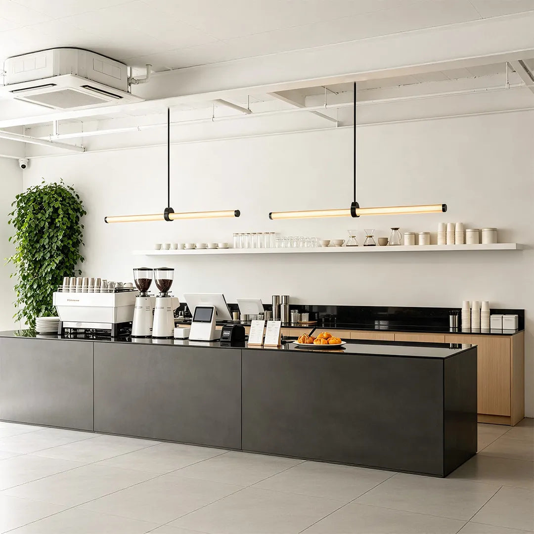 Linear pendant lights suspended above a minimalist cafe counter with open shelving.