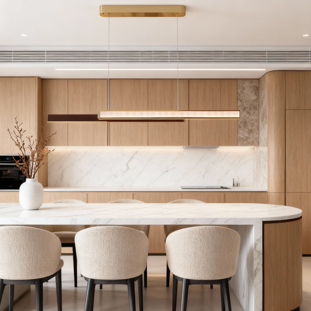 Gold linear suspension light installed above a bright kitchen island with wood cabinetry.