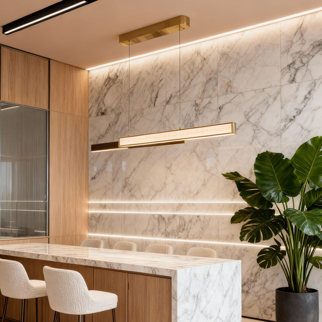 Gold linear suspension light illuminating a marble-and-wood kitchen with bar seating.