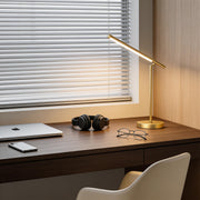 Linear table light with a sleek gold design, illuminating a modern wooden desk setup.
