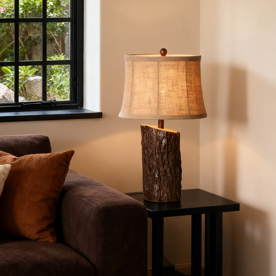 Lodge-style faux wood table lamp with a rough-hewn appearance, casting a warm glow on a black side table next to a sofa.