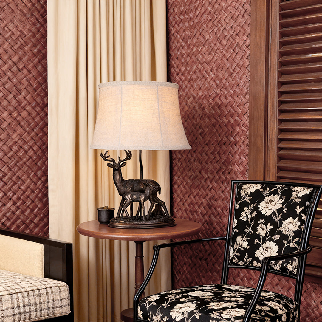 Lodge-style deer table lamp casting a warm glow on a round side table, complementing textured wallpaper and dark furnishings.