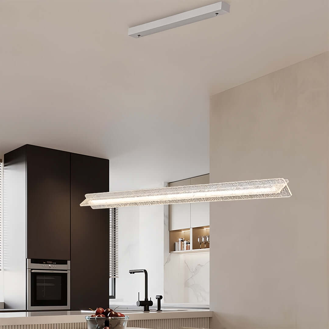 Long bar modern white pendant light fixture suspended over a dark-themed kitchen island in a minimalist apartment.