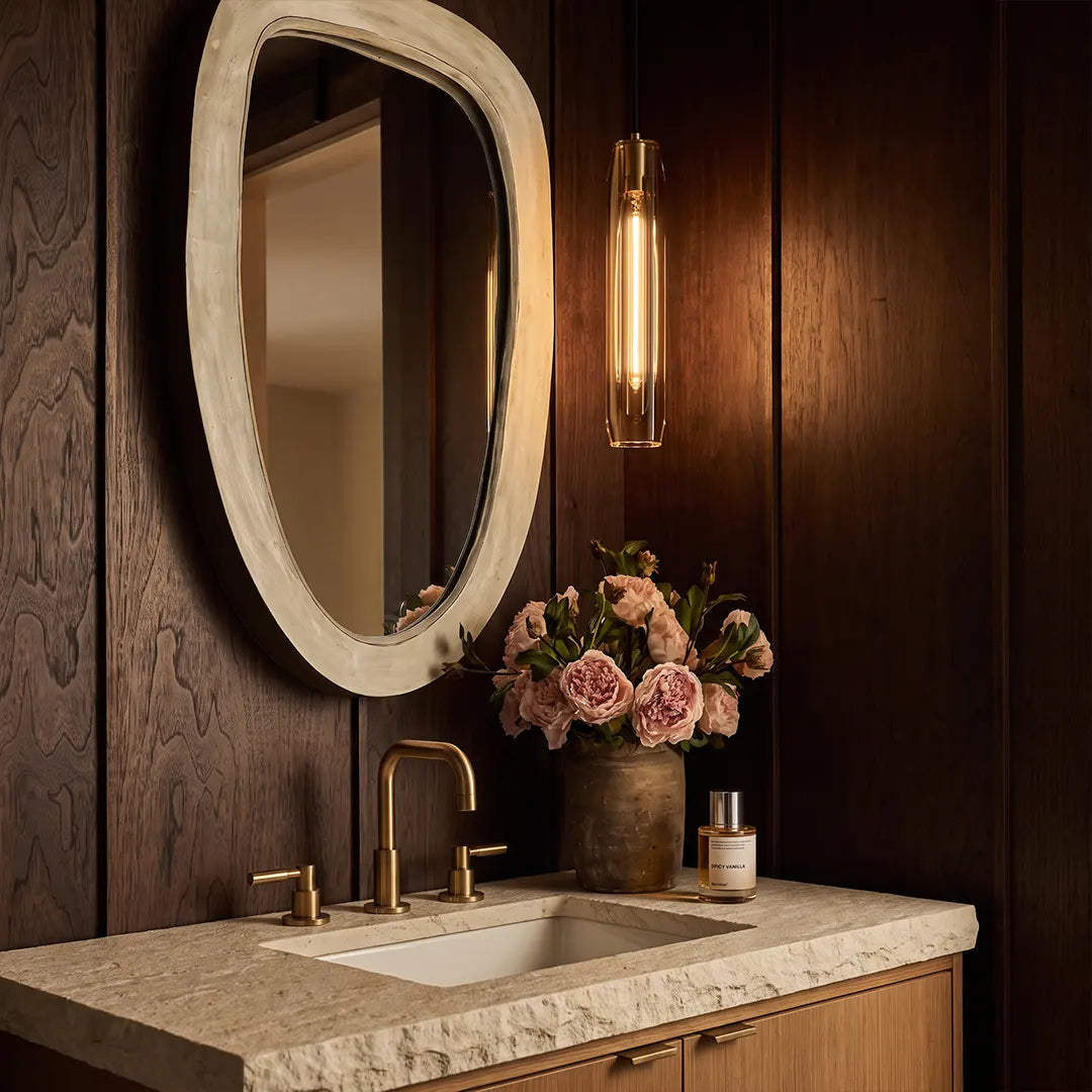 Long crystal pendant light installed beside a round mirror above a bathroom vanity in a warm elegant space.