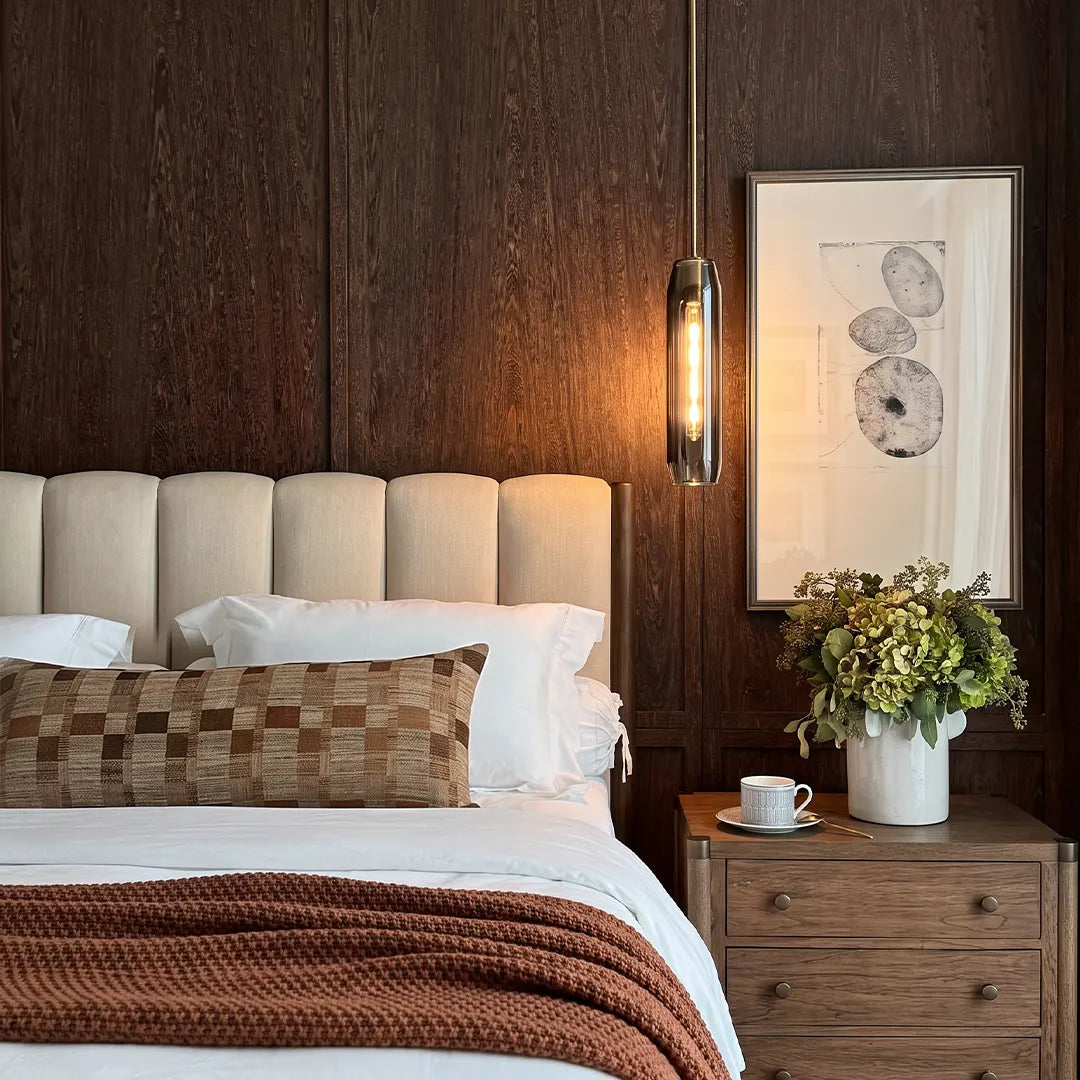 Long crystal pendant light hanging above a bedside table in a cozy bedroom with dark wood wall panels.