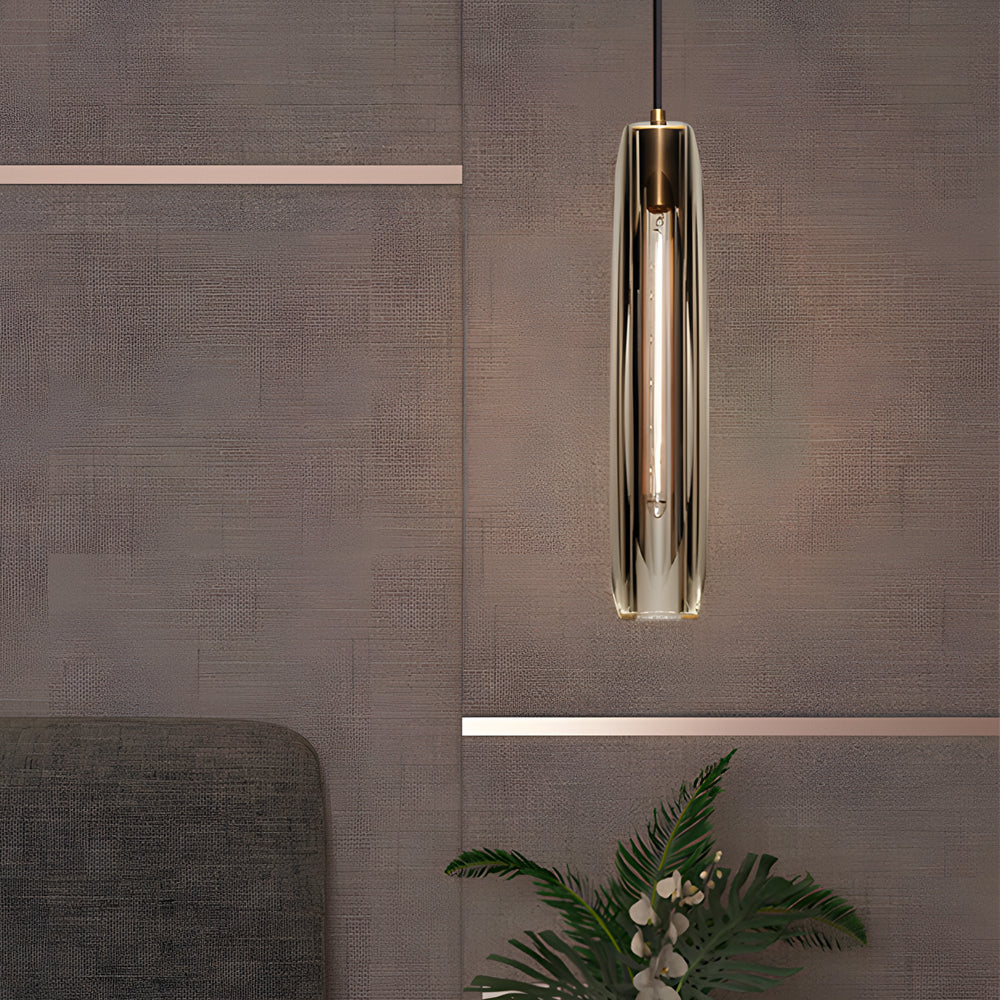 Long crystal pendant light with a slim cylindrical glass shade and warm gold finish suspended in a modern interior.