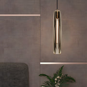 Long crystal pendant light with a slim cylindrical glass shade and warm gold finish suspended in a modern interior.