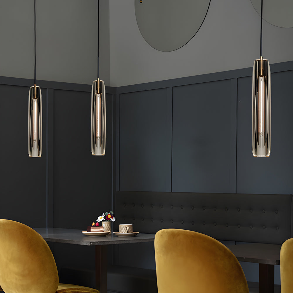 Long crystal pendant lights hanging over a dining table in a moody modern dining room with velvet chairs.