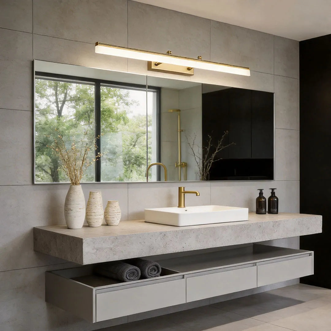Long gold bathroom vanity light fixture above a large mirror in a contemporary double sink bathroom.