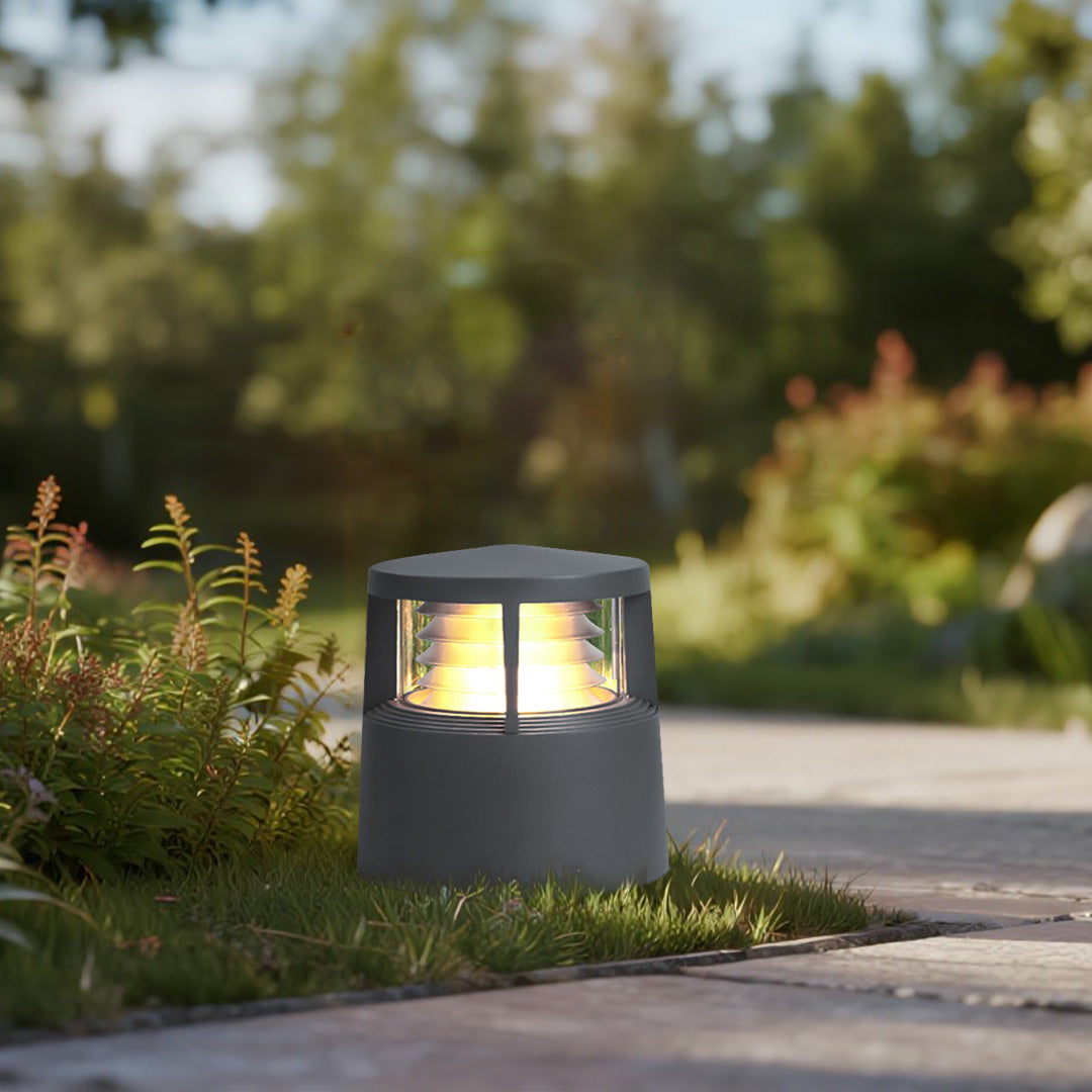 Round louvered bollard light emitting warm light in garden lawn