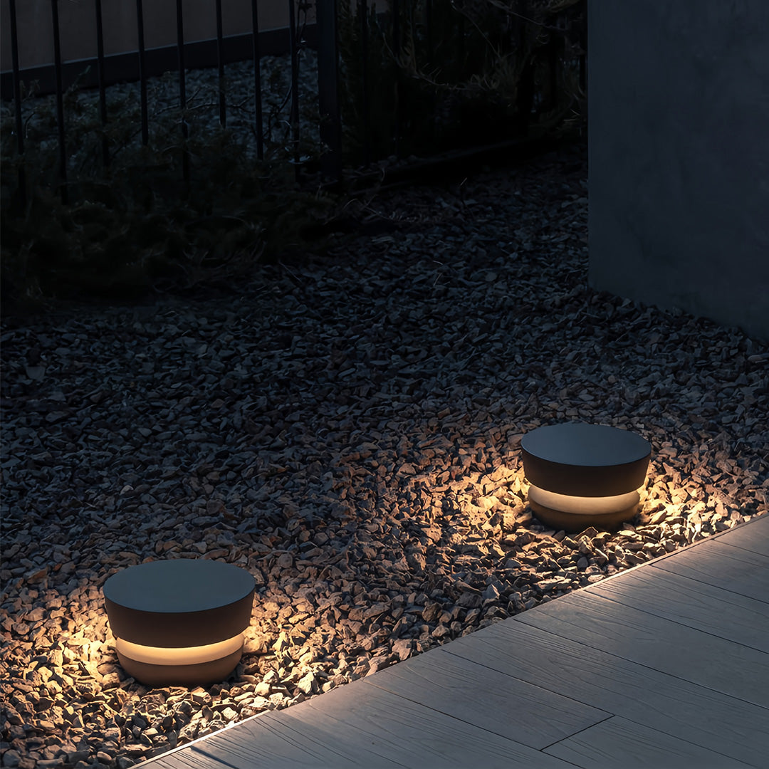 Low-level black pathway lights illuminating a dark gravel and stone bed, perfect for guiding visitors at night.