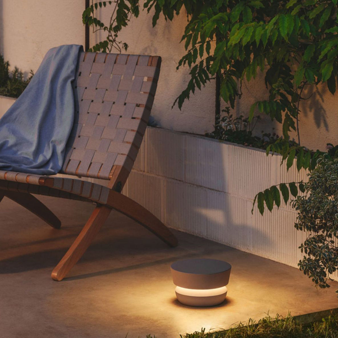 Low-profile black pathway lights illuminating a concrete patio next to a wooden outdoor chair and raised planter wall.