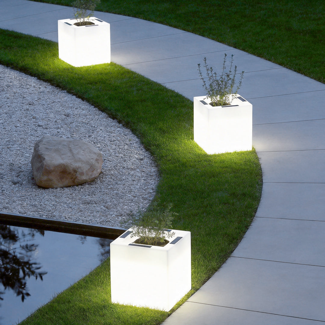 Luminous flower pots with a white finish, glowing in a garden pathway setting.