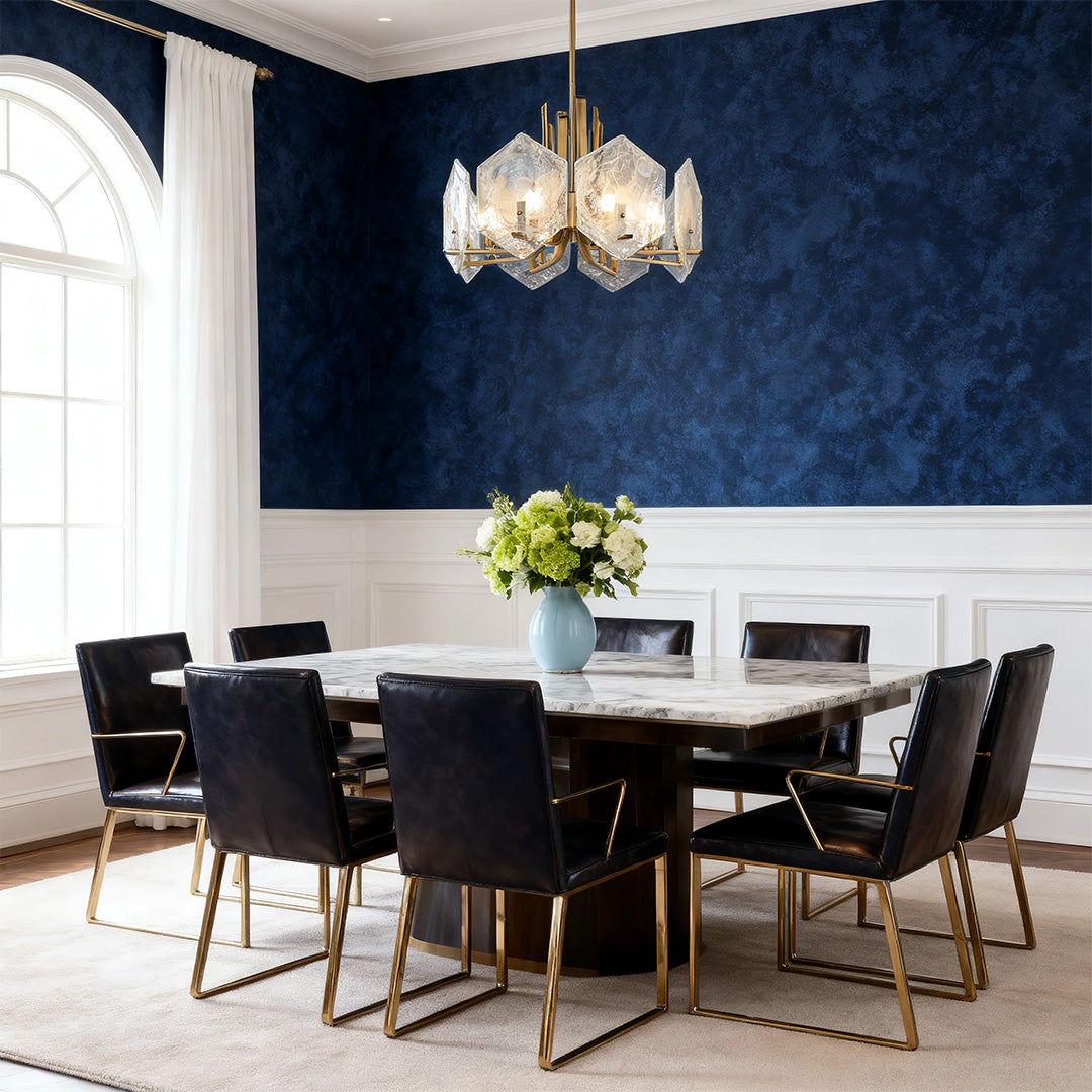 Luxurious setting with a gold geometric chandelier casting soft light on a long marble table and a textured navy accent wall.