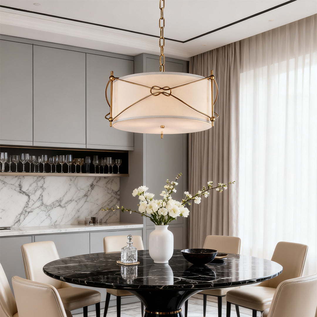 Luxury kitchen dining area with a contemporary white drum pendant light with brass detailing over a round black marble table.