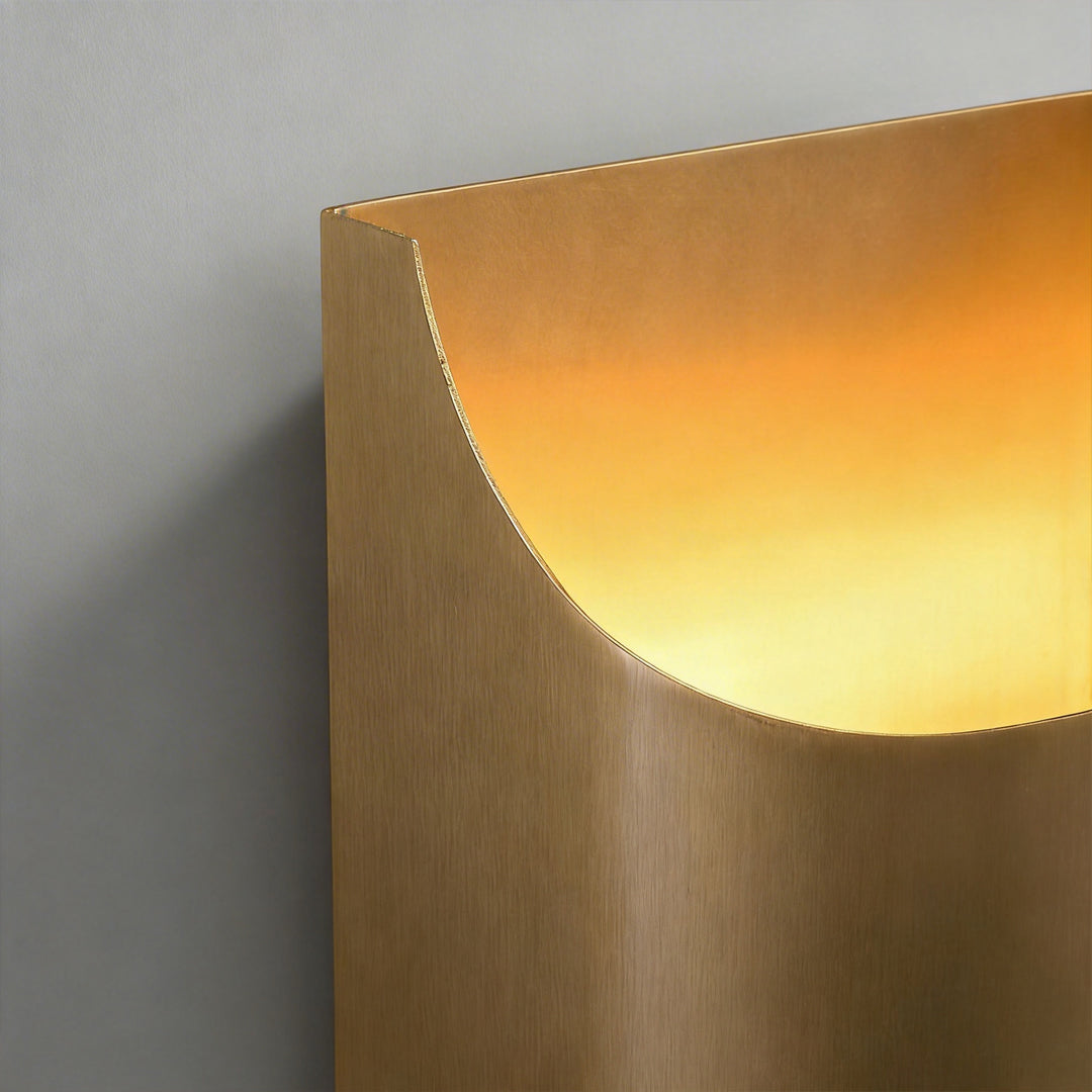 Macro detail of the brushed gold finish and curved edge of a brass wall light fixture at night.