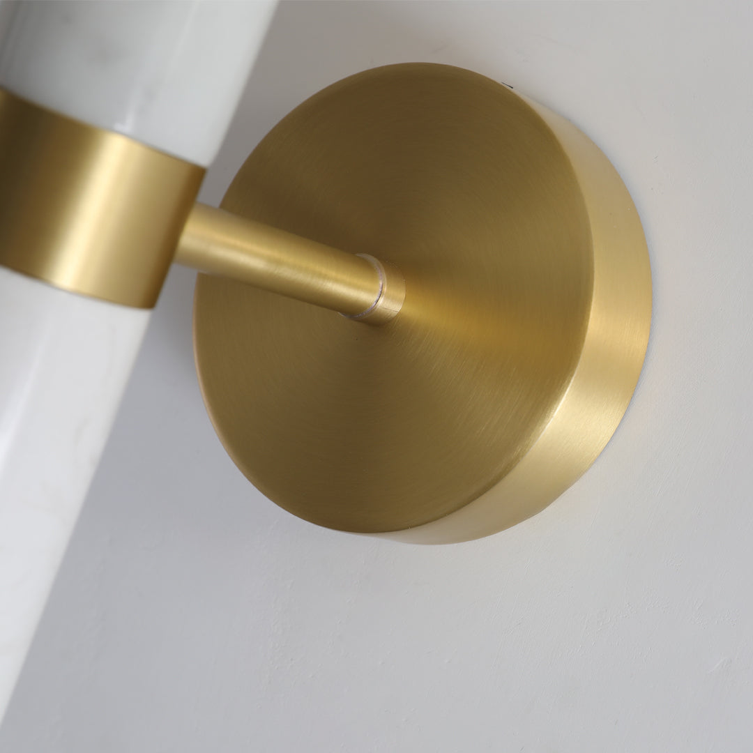 Macro detail of the brushed gold wall sconce lighting mounting plate and marble pillar arm.