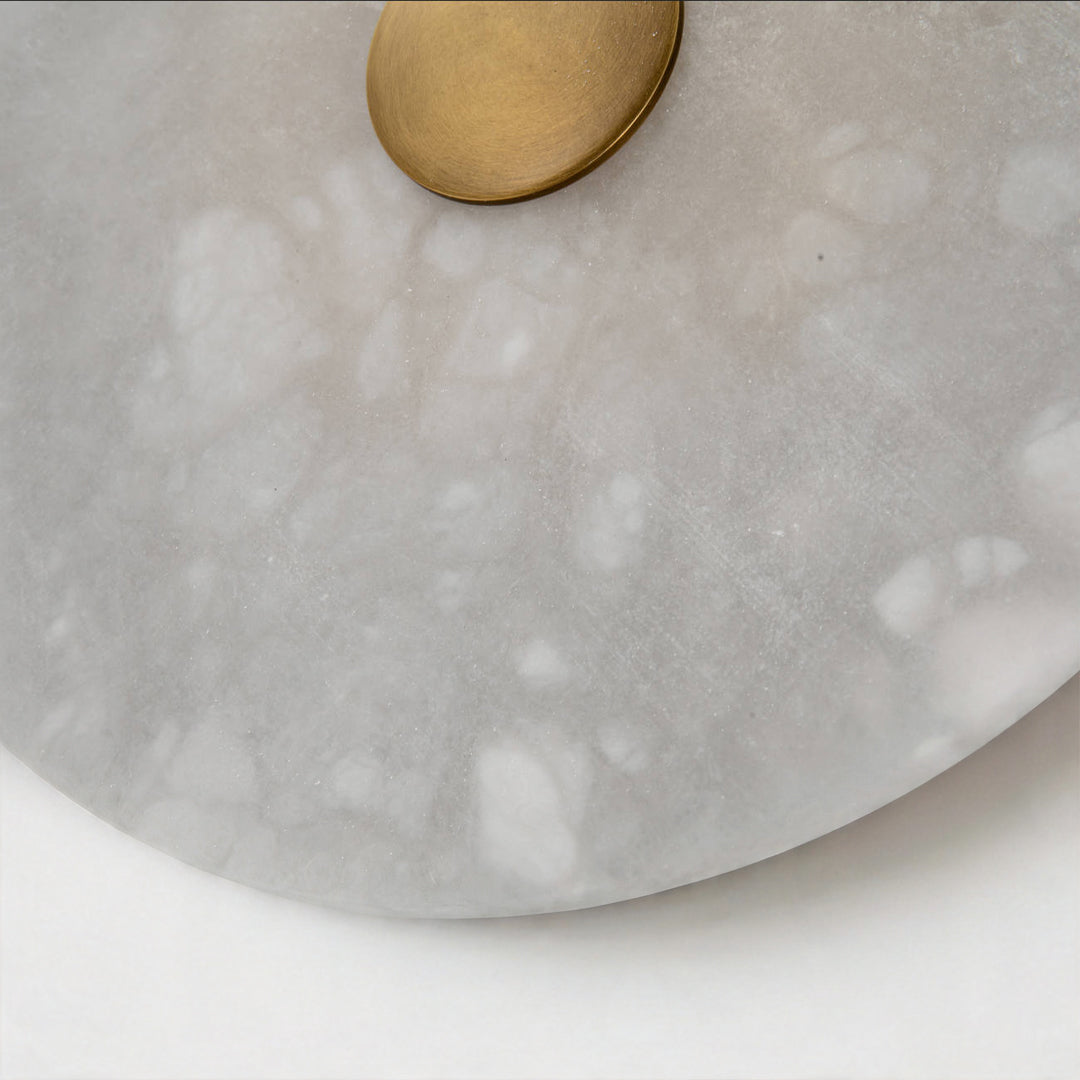 Macro detail of the grey marble texture and brass center of a round wall light fixture area.