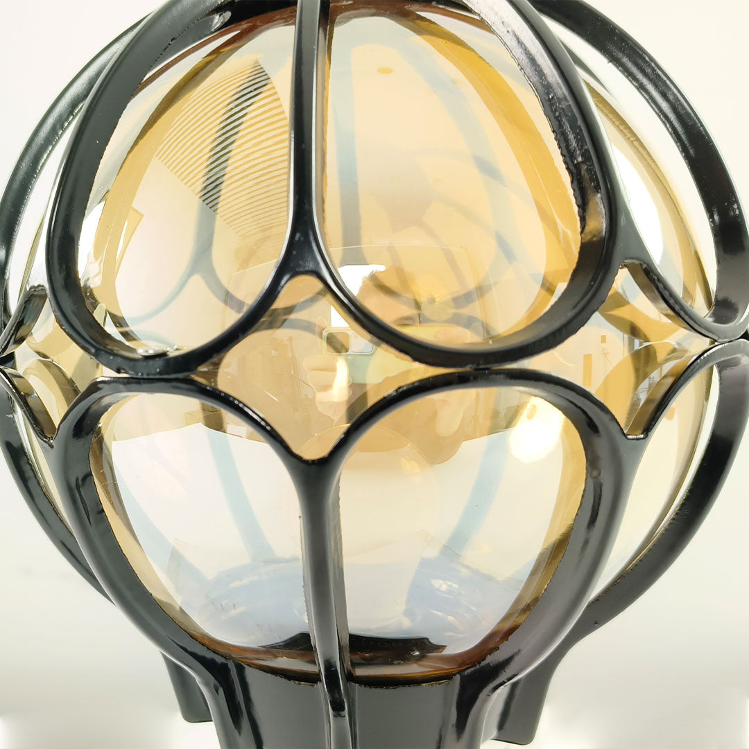 Macro close-up of the ornate black metal cage and amber glass on outdoor globe pillar lights ok.