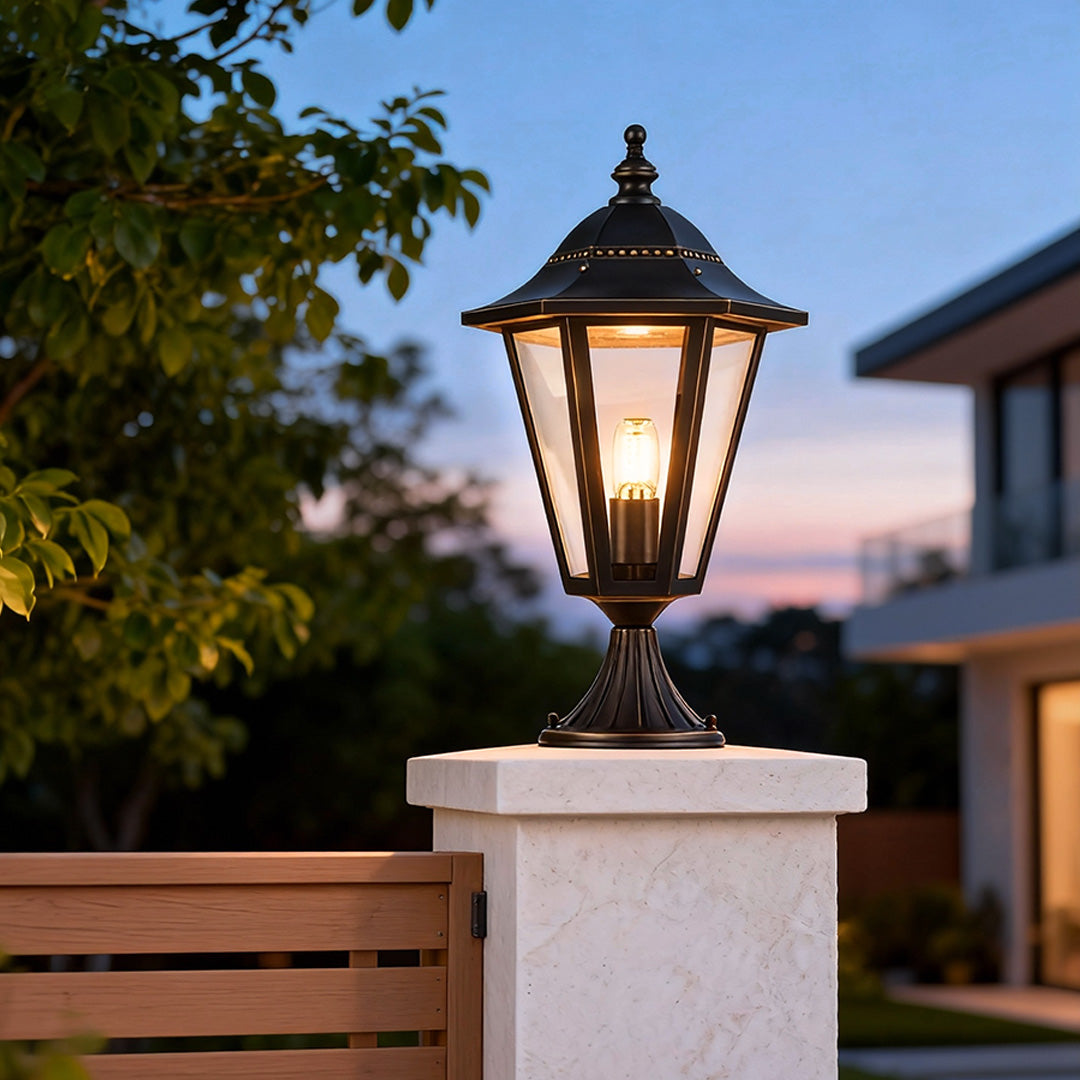 Main gate pillar light illuminating a stone pillar beside a tropical garden at dusk.