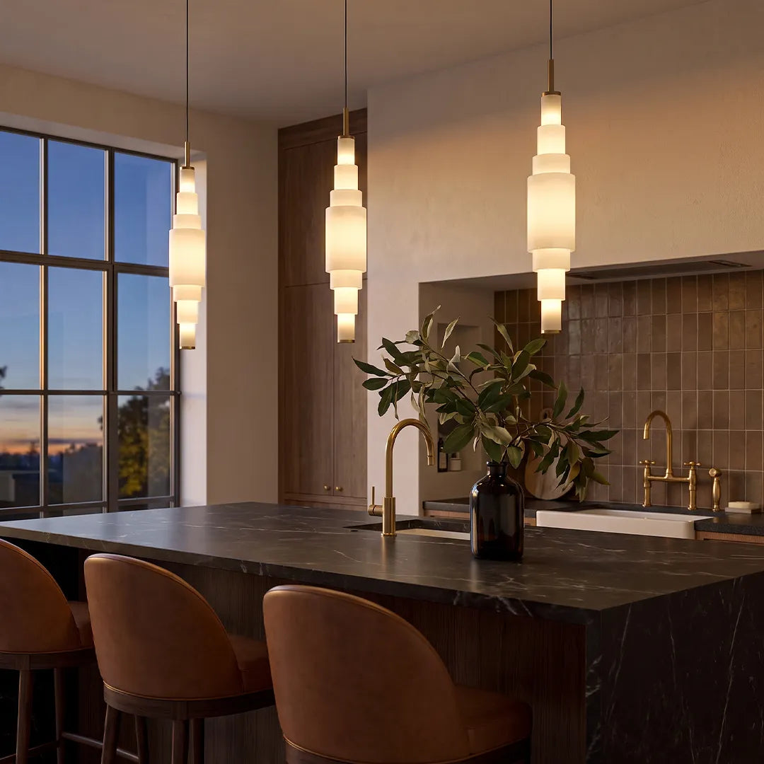 Marble chandelier suspended above a kitchen island with dark countertops and upholstered stools.