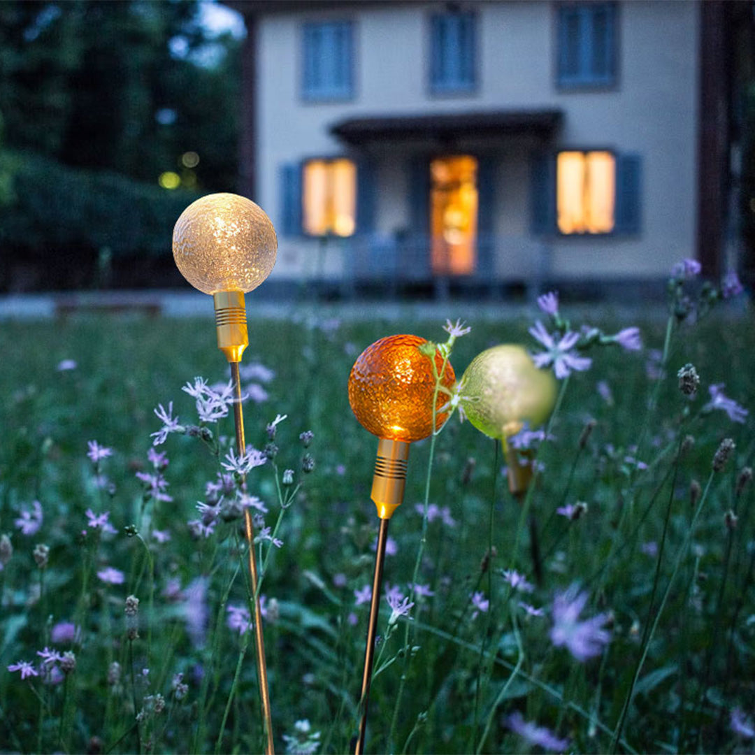 Golden crackle-glass globe stake lights illuminating a soft garden meadow for path landscape lighting.