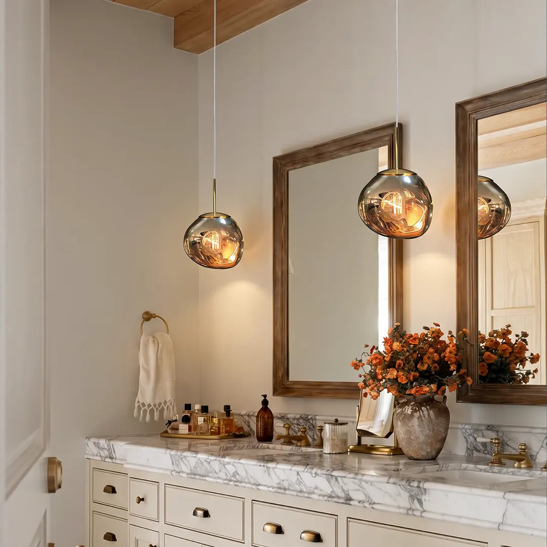 Melt pendant light with a glossy amber globe shade suspended above a marble vanity in an elegant bathroom.